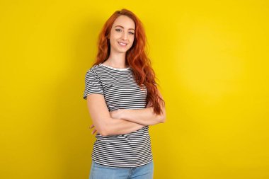 Sarı arka planda çizgili tişört giyen kızıl saçlı kadının portresi katlanır kolları ve gülümseyen
