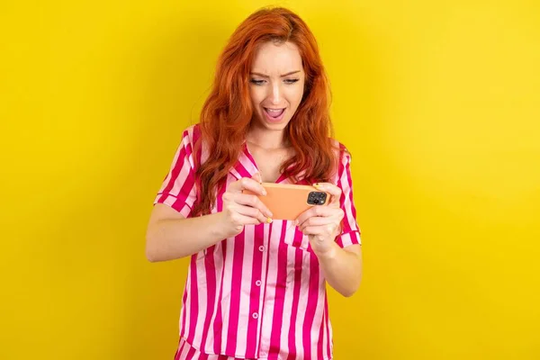 Портрет Возбужденной Молодой Рыжей Женщины Розовом Пижаме Играющей Игры Мобильном — стоковое фото
