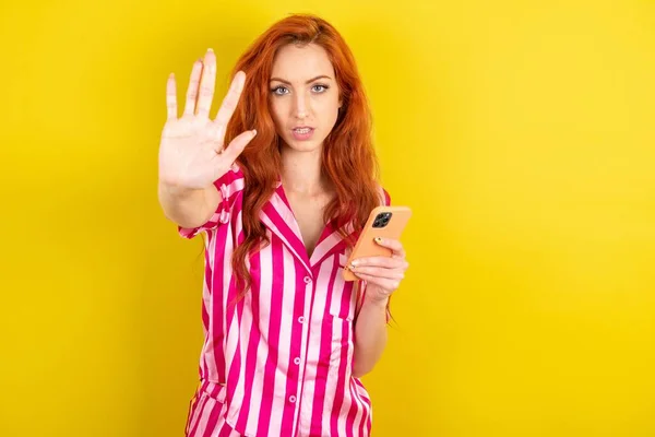 woman using and texting with smartphone with open hand doing stop sign with serious and confident expression, defense gesture