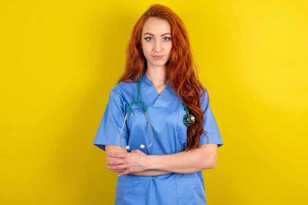 自信严肃 红头发 身披黄褐色背景的女医生双手交叉地站在那里 显示出专业的激情站在自信的立场上 — 图库照片