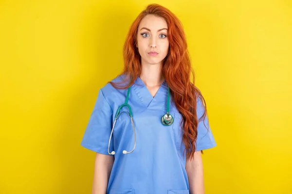 一个红头发的年轻女医生在黄色工作室的背景下惊慌失措地凝视着令人震惊的消息 被石头砸死的女人屏住呼吸 — 图库照片