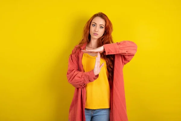 イエロースタジオの背景の上に立っている美しい赤毛の女性は タイムアウトジェスチャーを示す動揺している 必要性停止 ハードワーク後に休息のための時間を求める — ストック写真