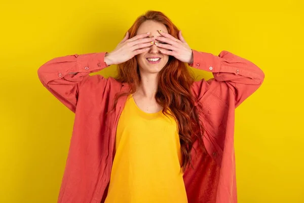 美丽的红头发女人站在黄色工作室的背景上 双手捂住眼睛 笑容满面 笑逐颜开 盲目概念 — 图库照片