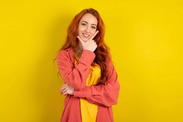 黄色いスタジオの背景に立っている美しい赤毛の女性は 交差した腕と手で笑顔でカメラに自信を持って見ています ポジティブに考える — ストック写真