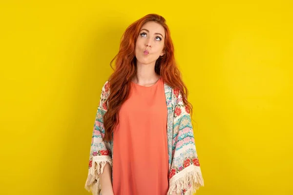 stock image red haired woman standing over yellow studio background making fish face with lips, crazy and comical gesture. Funny expression.