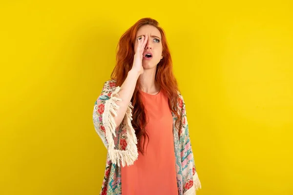 stock image red haired woman standing over yellow studio background shouting and screaming loud to side with hand on mouth. Communication concept.