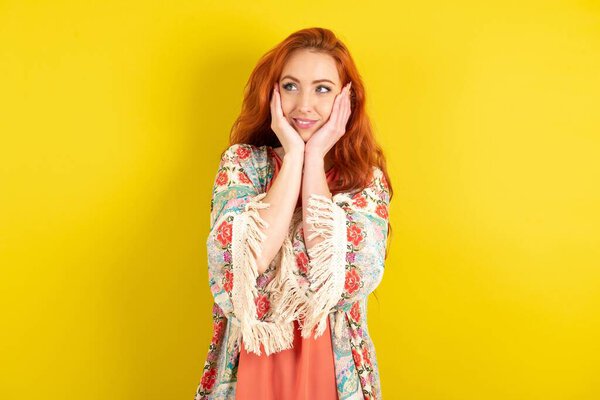 Inspired red haired woman standing over yellow studio background looking at copyspace having thoughts about future events