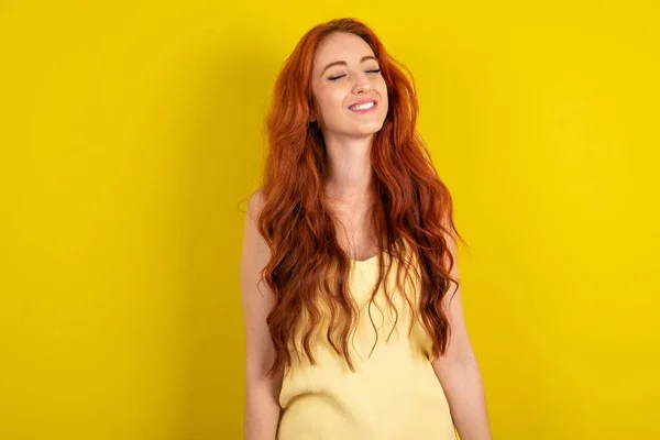 漂亮的红头发女人 穿着黄色的衬衫 背景是黄色的 满脸喜色 闭上双眼 笑着露出完美的白牙 — 图库照片