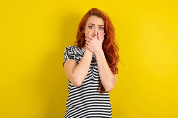 Ошеломленная Рыжеволосая Женщина Полосатой Рубашке Жёлтом Фоне Студии Закрывает Рот — стоковое фото