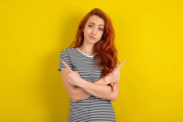 Roodharige Vrouw Met Gestreept Shirt Gele Studioachtergrond Kruist Armen Punten — Stockfoto