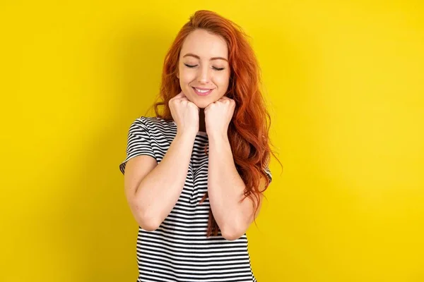 黄色いスタジオの背景にストライプシャツを着ている陽気な赤毛の女性は 静かな満足の表情 白い歯 人々の感情を示しています — ストック写真