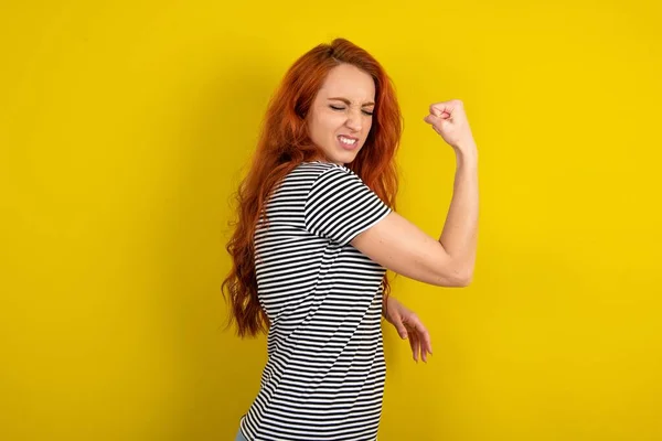 黄色工作室背景下穿着条纹衬衫的滑稽红头发女人的肖像欢呼是啊举起拳头庆祝胜利游戏比赛 — 图库照片