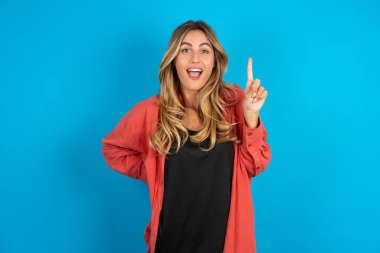 Sarışın kadın tişört giyiyor, parmağını kaldırıyor fikir üretiyor ve poz veriyor.