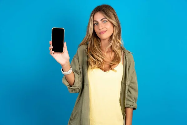 파란색 배경에 셔츠를 여자는 새로운 전화를 신비로운 셀룰러의 디스플레이 — 스톡 사진