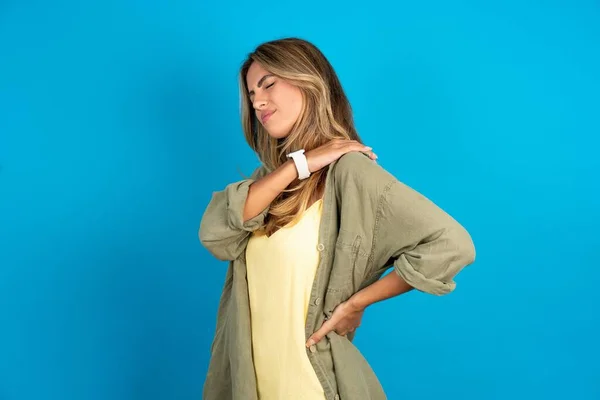 Schöne Blonde Frau Trägt Overshirt Auf Blauem Hintergrund Bekam Rückenschmerzen — Stockfoto