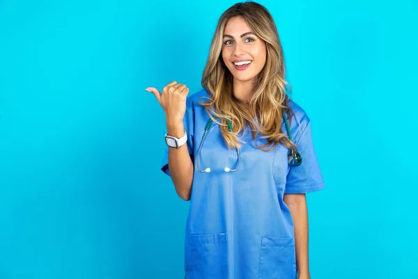 漂亮的医生女士站在蓝色工作室的背景上 用食指指尖着一边 在复制的空间里展示着便宜货的消息 — 图库照片