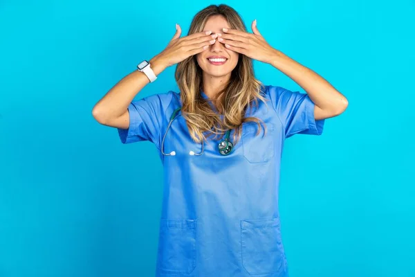 青いスタジオの背景の上に立っている美しい医師の女性は 笑顔で面白い手で目を覆います ブラインドコンセプト — ストック写真