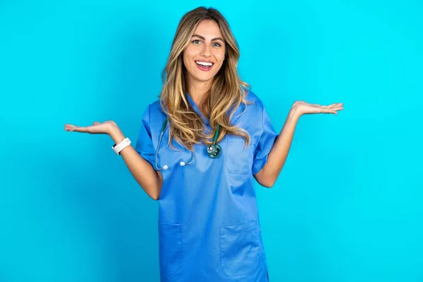 快乐快乐乐观美丽的医生女人站在蓝色工作室的背景上 双手拿着复制的空间 — 图库照片