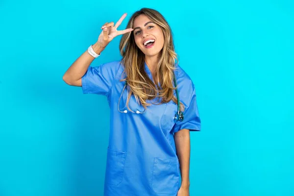 Bela Médico Mulher Sobre Fundo Estúdio Azul Fazendo Símbolo Paz — Fotografia de Stock