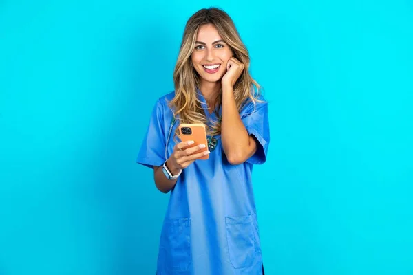 Radostná Krásná Lékařka Stojící Nad Modrým Studiem Pozadí Pózuje Mobilním — Stock fotografie