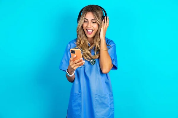 站在蓝色工作室背景上的美丽快乐的医生女士在智能手机屏幕上的时候感觉很好 生活方式 — 图库照片