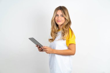 Beyaz arka planda futbol tişörtü giyen iyimser güzel bir kadının fotoğrafı tablet içeriyor