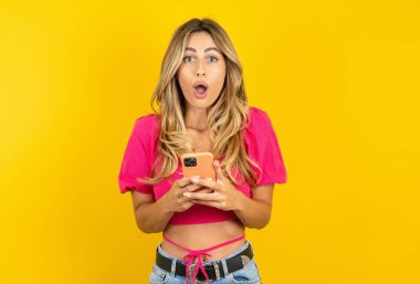 Şok olmuş, sarı arka planda pembe etek giyen genç bir kadın ağzı açık, telefon ahizesi okuyor inanılmaz büyük alışveriş reklamları yapıyor. 