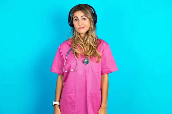 ピンクの医療ユニフォームの不満な慎重な白人女性の医師は 顔がヘッドフォンで不満を感じる — ストック写真