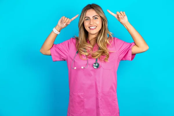 穿着粉色医疗制服的疯狂的高加索女医生的照片 听诊器指向头发 — 图库照片