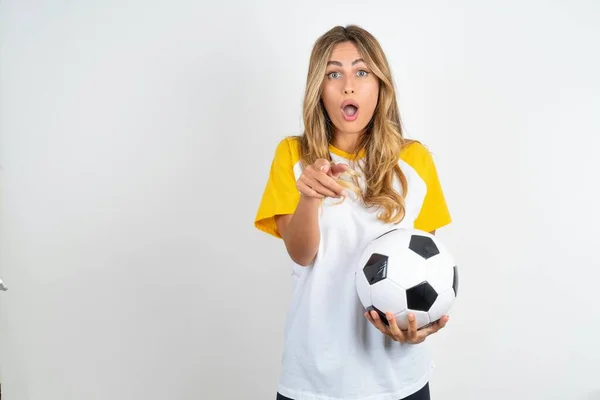 Zszokowana Młoda Piękna Kobieta Trzyma Piłkę Nożną Nad Białymi Punktami — Zdjęcie stockowe