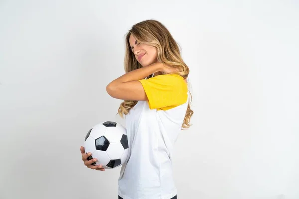 beautiful woman wearing football T-shirt over white background got back pain holding  soccer ball