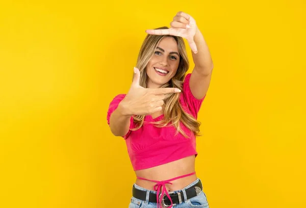 Młoda Blondynka Ubrana Różową Bluzkę Żółtym Tle Robi Palców Ramkę — Zdjęcie stockowe
