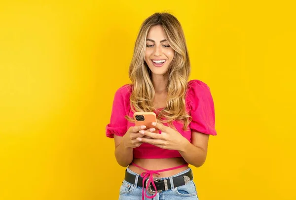 年轻的金发女子 黄色背景 头戴粉色麦片 在空闲时间用手机聊天 — 图库照片