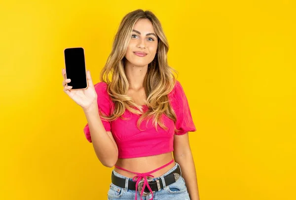 漂亮的金发碧眼的年轻女子 头戴粉色的庄稼顶盖 黄色背景 带着空白屏幕的手机 — 图库照片