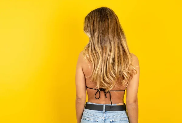 黄色の背景にビキニを着用している美しい若い金髪の女性のバックビュー スタジオシュート — ストック写真