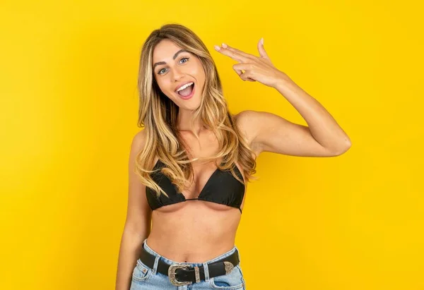 Sarı Arka Planda Bikini Giyen Güzel Sarışın Kadın Parmak Tabancası — Stok fotoğraf
