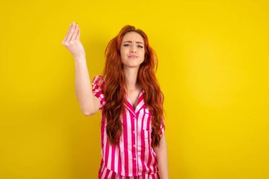 Sarı arka planda pembe pijama giyen genç kızıl saçlı kadın tipik İtalyan jestleri yapıyor, kameraya bakıyor.