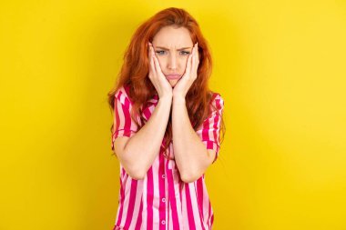 Sarı arka planda pembe pijama giyen kızıl saçlı kadın. Yüzü, depresyonu ve üzüntüyü örten yorgun eller.