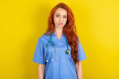 Tatminsiz genç, kızıl saçlı doktor kadının portresi sırıtıyor, dudakları kesiliyor ve kameraya rahatsız edici bir şekilde bakıyor, tatsız bir şey duymaktan hoşnutsuzluk duyuyor.