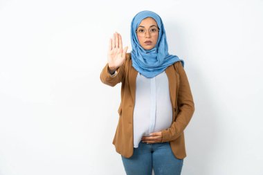 Başörtüsü takan müslüman hamile kadın avuç içiyle şarkı söylemeyi kesiyor. Yüzünde olumsuz ve ciddi bir jest olan uyarı ifadesi.