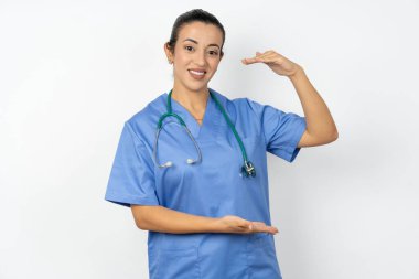 Arap doktor kadın mavi üniformalı, elleri büyük ve büyük boy işareti gösteren, ölçü sembolü olan. Kameraya bakıp gülümsüyor..