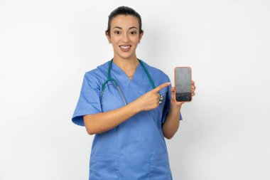 Mavi üniformalı gülümseyen Arap doktor kadın boş ekranla cep telefonunu işaret ediyor.