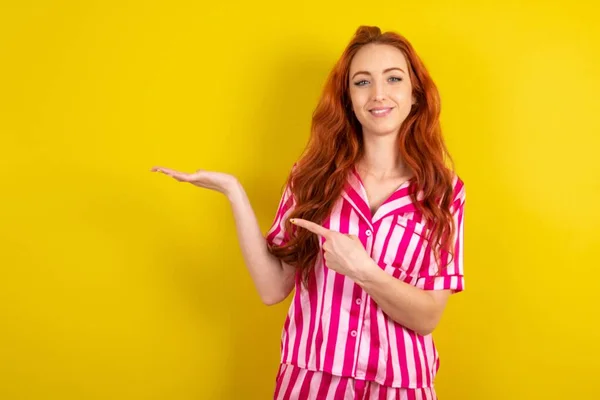 Mujer Pelirroja Con Pijama Rosa Sobre Fondo Estudio Amarillo Apuntando — Foto de Stock