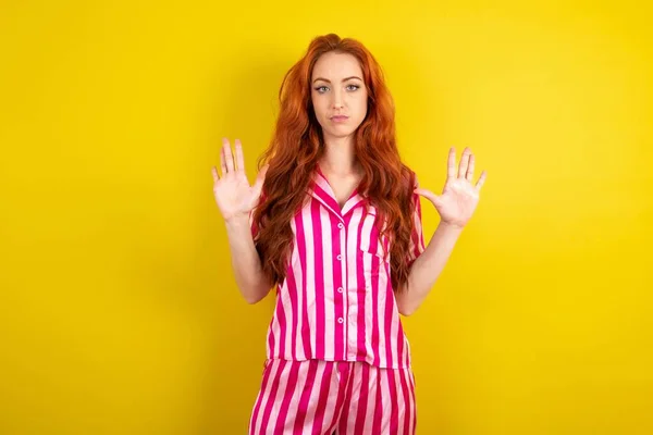 Serieuze Roodharige Vrouw Draagt Roze Pyjama Gele Studioachtergrond Trekt Handpalmen — Stockfoto