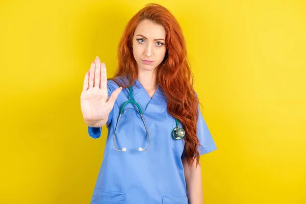 年轻红头发的医生女士展示了停车标志禁止通行标志 手心紧握着相机 表情严肃 — 图库照片