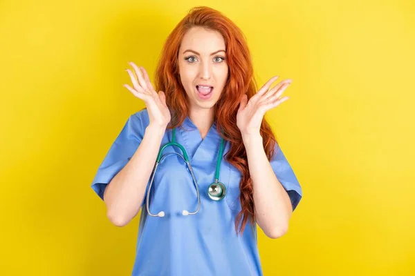 Surprised young red-haired doctor woman , glad to see big discounts on clothes, expresses shock, keeps hands near head, jaw dropped.