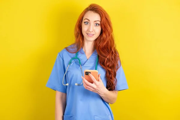 Ung Rödhårig Läkare Kvinna Håller Mobiltelefon Händerna Och Glädjer Sig — Stockfoto