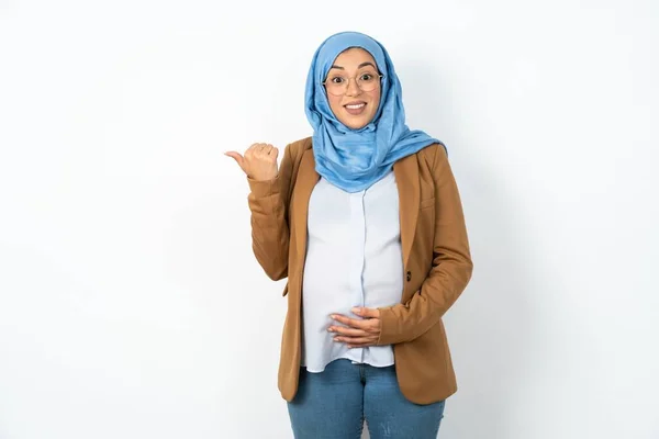 美しいイスラム教徒の妊婦は 先頭を指してヒジャーブを着て 交渉についてのニュースを持っているコピースペースで示しています — ストック写真