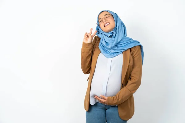 イスラム教徒の妊婦は 勝利の標識をしているカメラでハッピーフェイスウィンキングで笑顔でヒジャーブを着ています ナンバー2 — ストック写真
