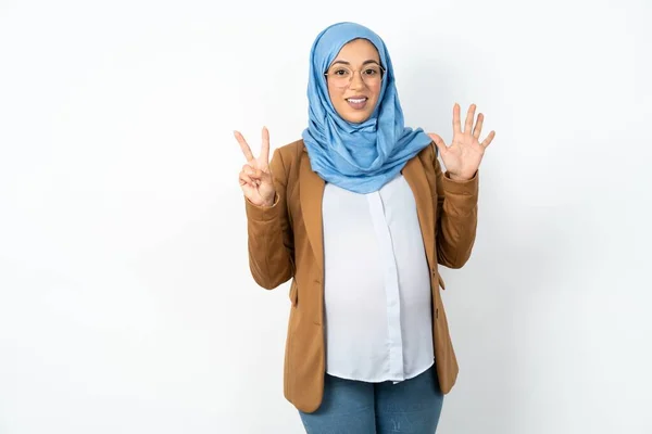 ヒジャーブを身に着けているイスラム教徒の妊婦は自信と幸せを笑いながら指ナンバー7を指で指で指さす — ストック写真